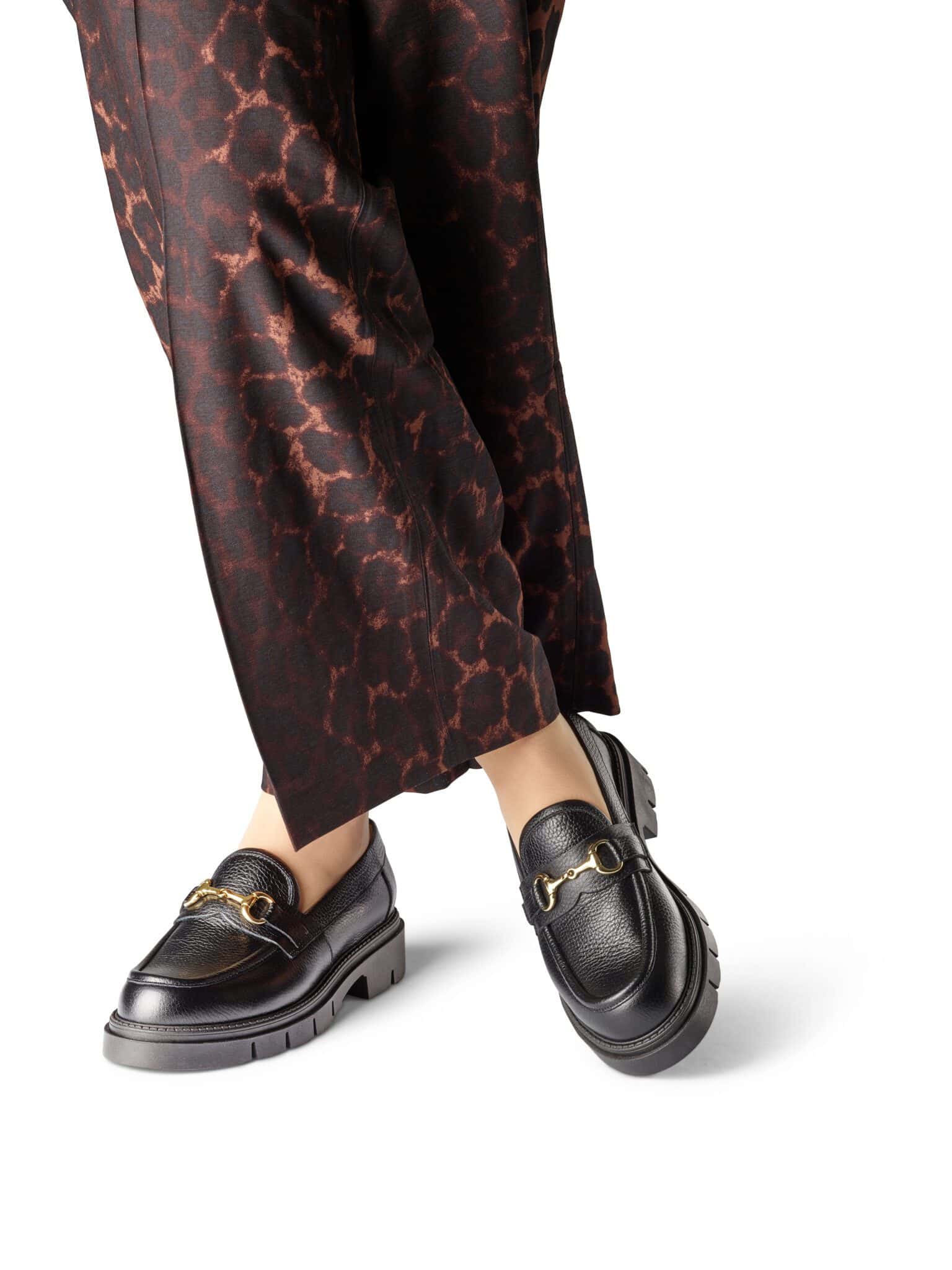 Svarta loafers med gulddetaljer och leopardmönstrade byxor.