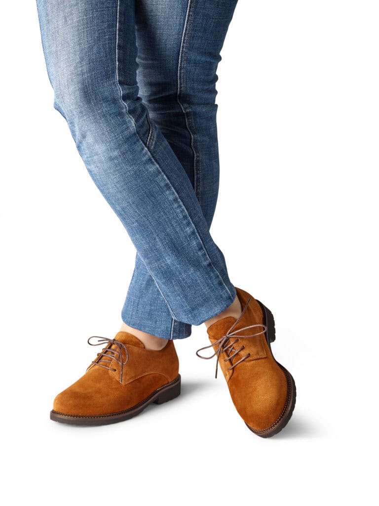 Damfötter i brunt läder och blå jeans, nära bildfokus.