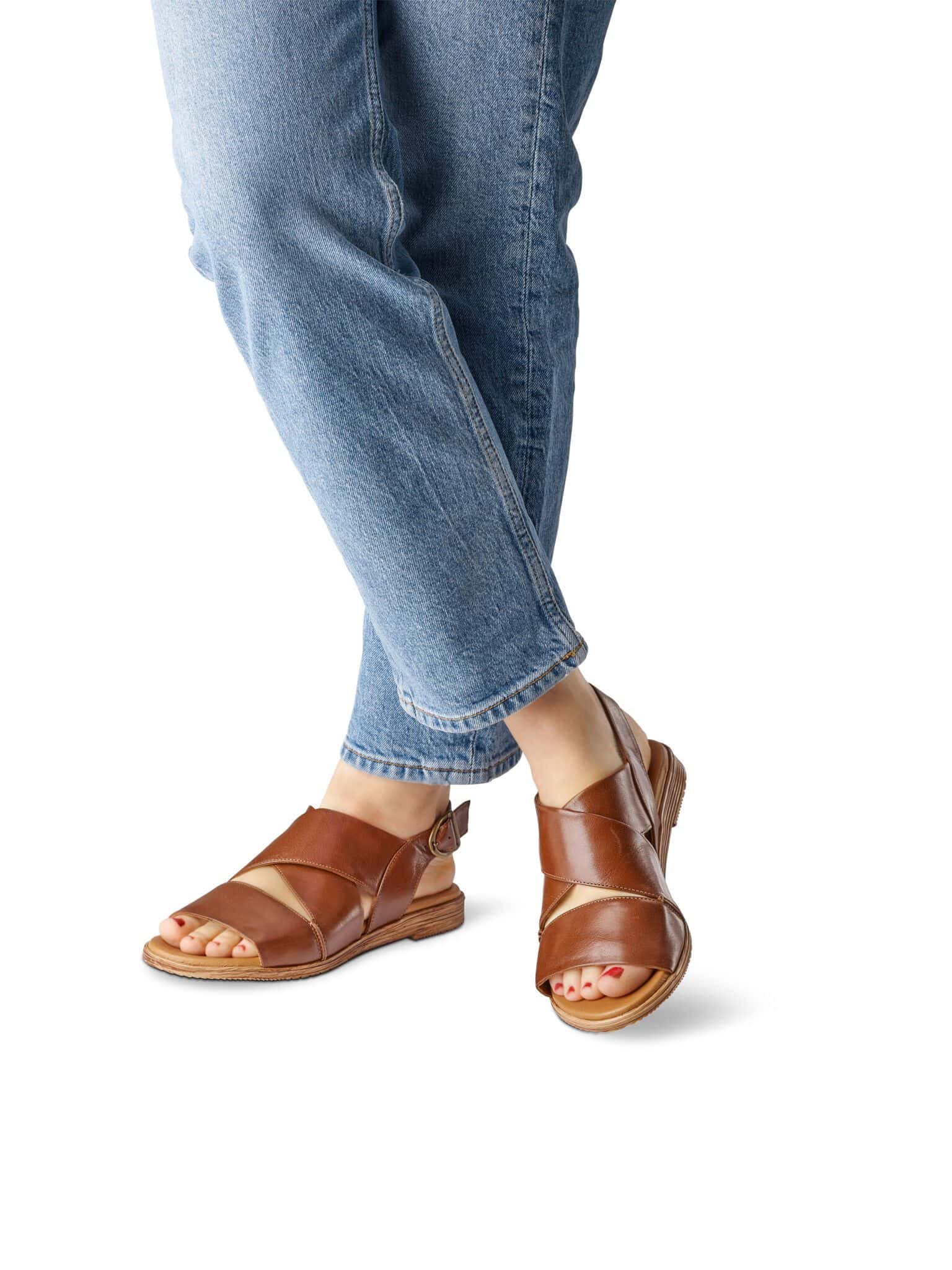 Damfötter i bruna sandaler och jeans, nära bildens botten.