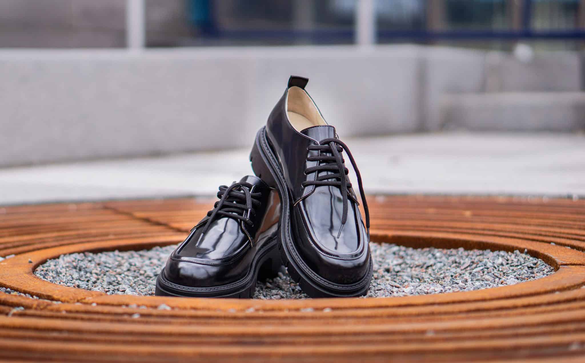 Svarta läderskor placerade på en träbänk utomhus.