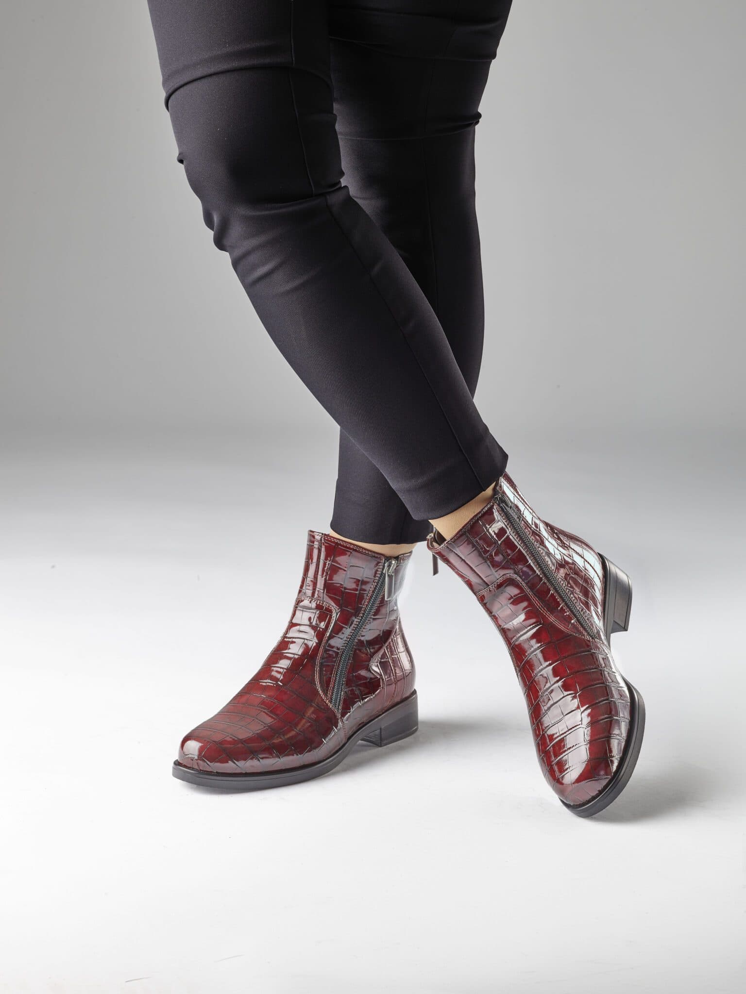 Damfötter i röda läderstövlar och svarta byxor mot en neutral bakgrund.