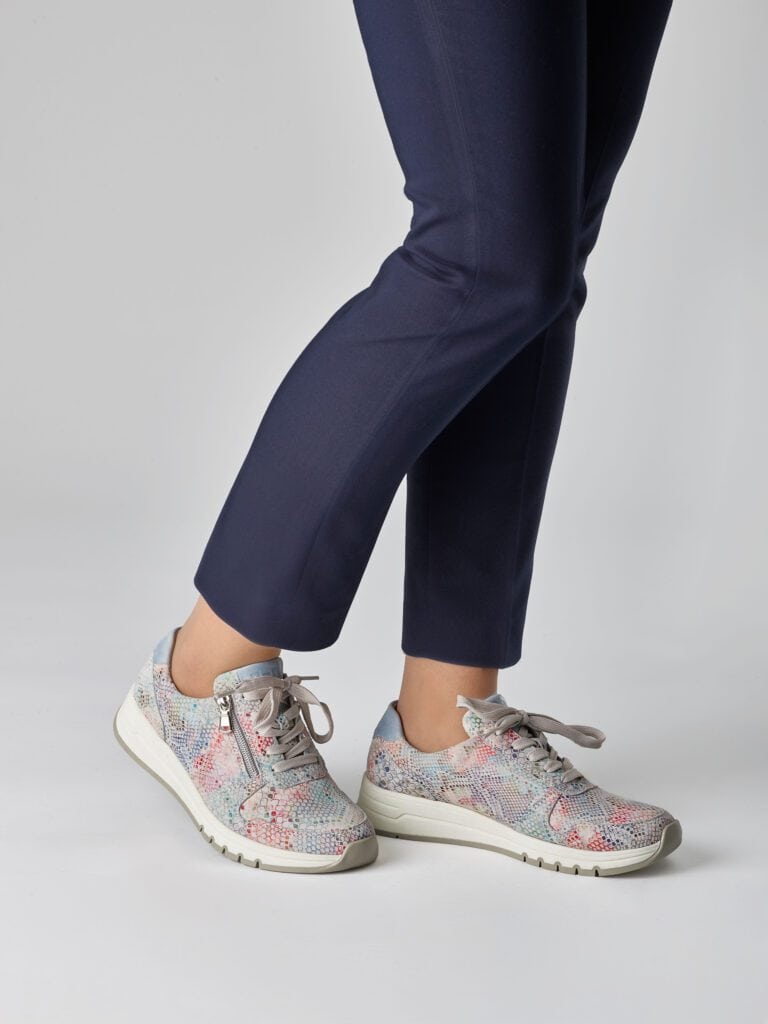 Damfötter i mönstrade sneakers och mörkblå byxor mot ljus bakgrund.